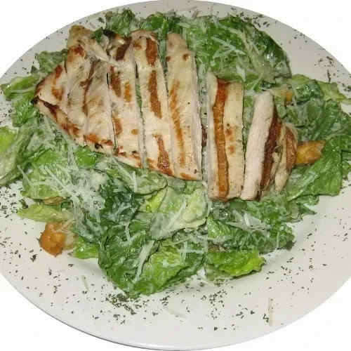 Grilled chicken Caesar salad with parmesan cheese on a white plate.