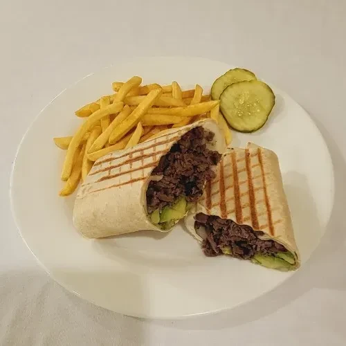 A beef and avocado wrap with fries and pickles on a white plate.