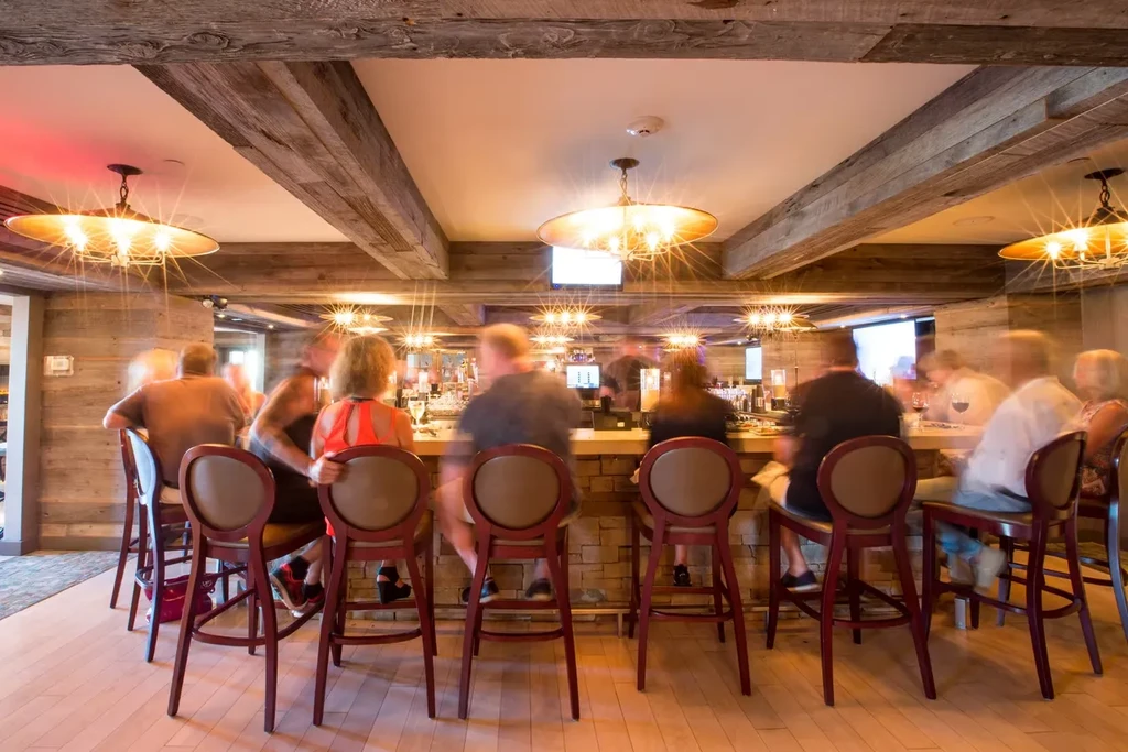 Warm restaurant bar with wooden beams, chandeliers, and blurred patrons.