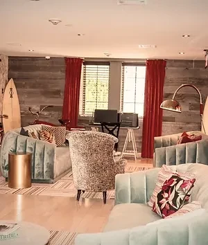 Eclectic lounge with blue sofas, patterned armchair, surfboard, and vintage bicycle.