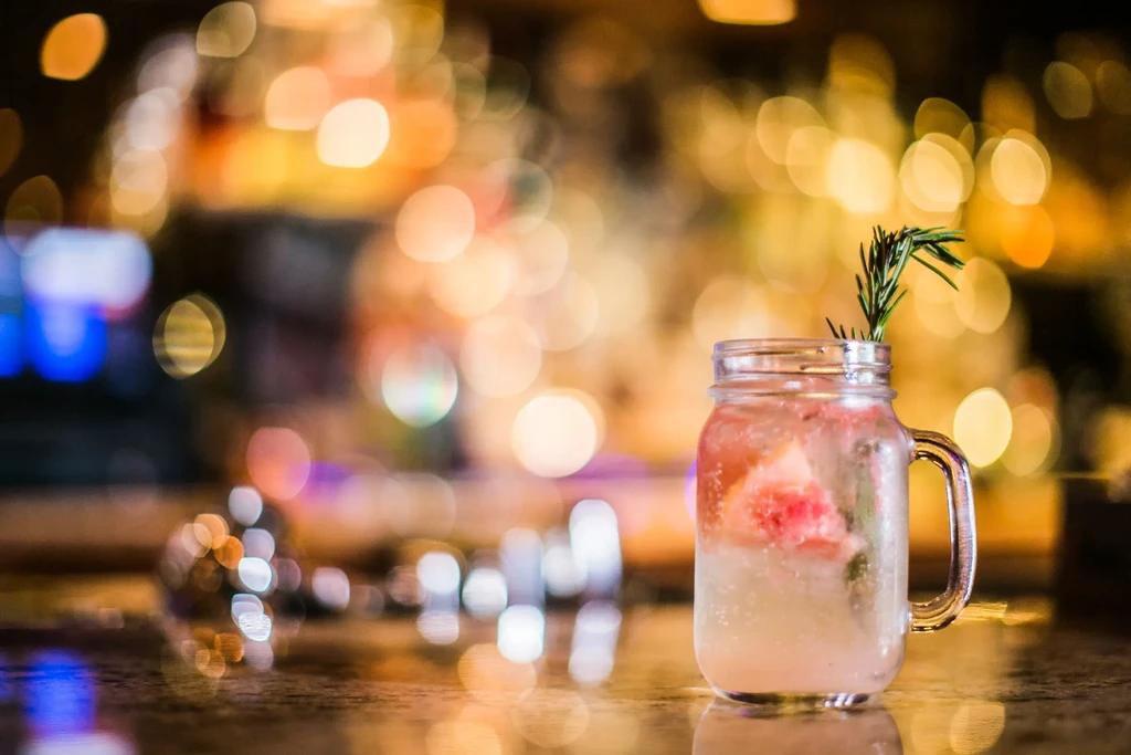 Iced pink cocktail with rosemary and citrus in a mason jar.
