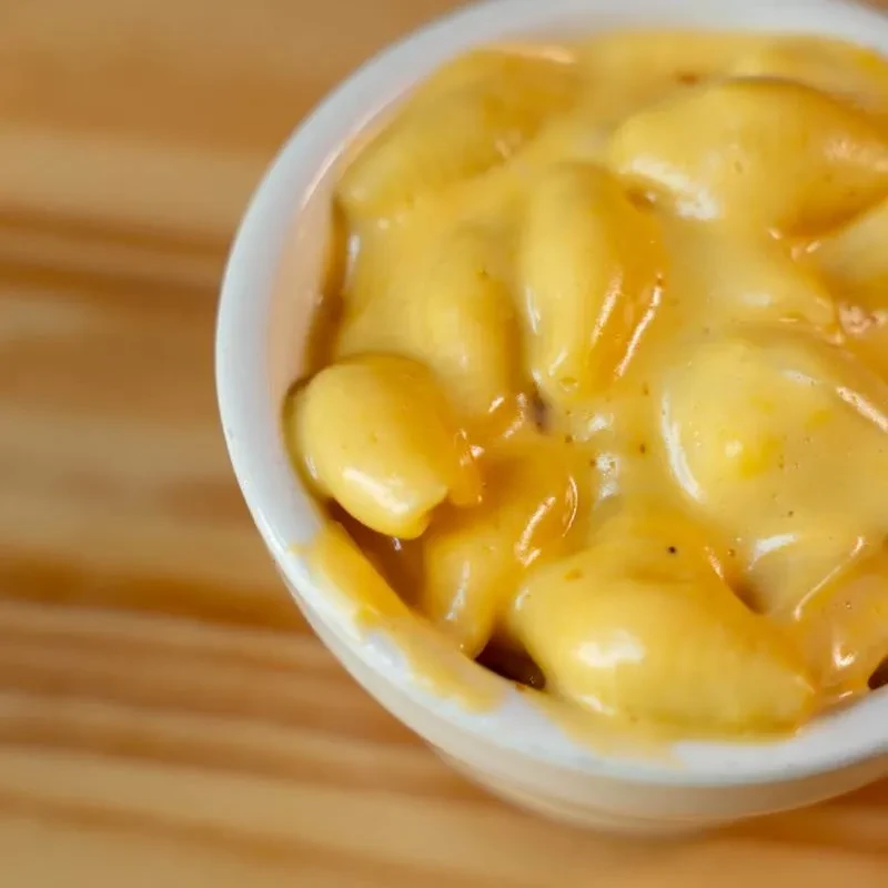 White bowl of creamy, orange-yellow macaroni and cheese with seasoning.