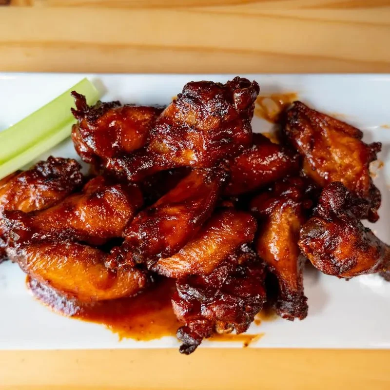 Close-up of glossy chicken wings with celery on a white plate.