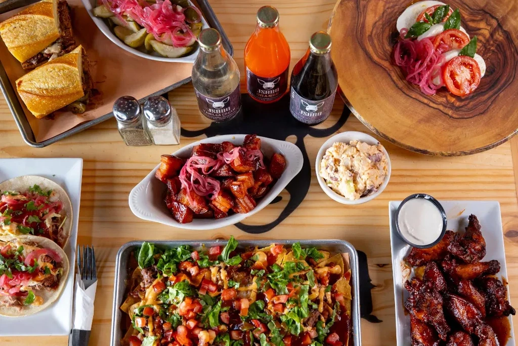Overhead view of various BBQ dishes: tacos, nachos, wings, sodas.