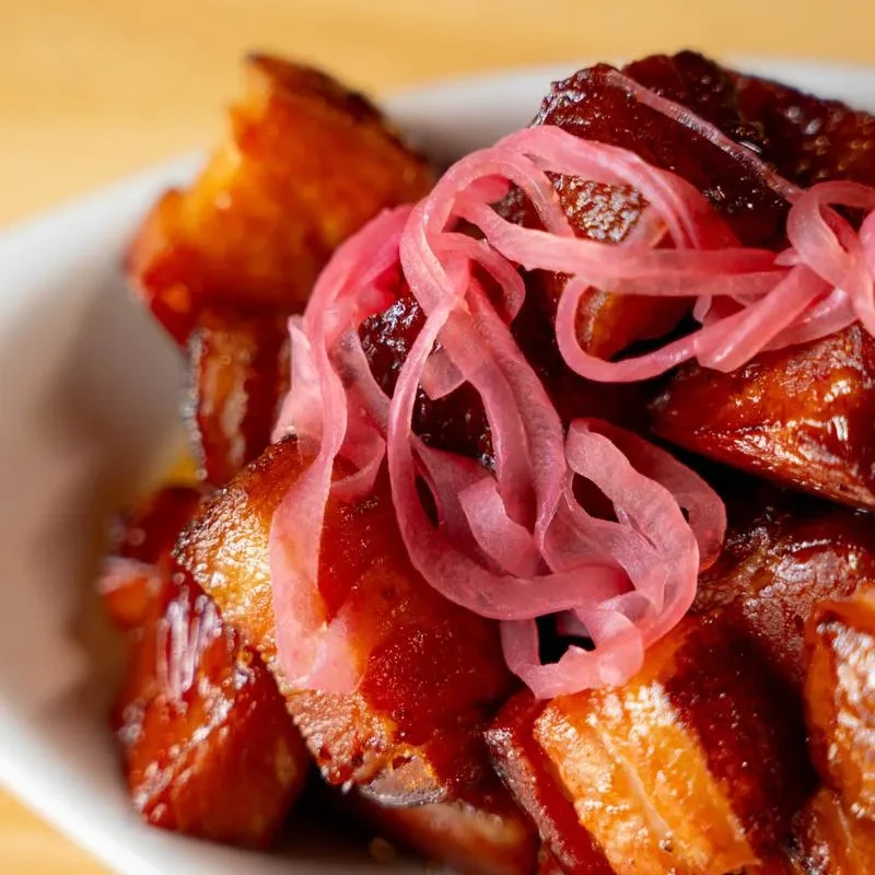 Braised pork belly with dark glossy sauce and pink pickled onions.
