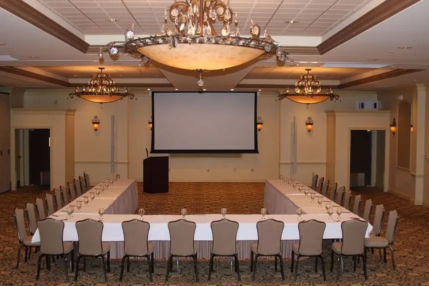Empty, elegant meeting room with U-shaped table, podium, and chandeliers.