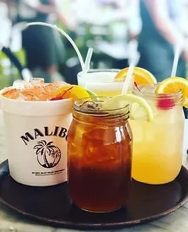 Four colorful iced beverages, including a Malibu bucket, with fruit garnishes.