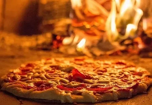 Uncooked pizza with cheese and peppers in a fiery wood-fired oven.