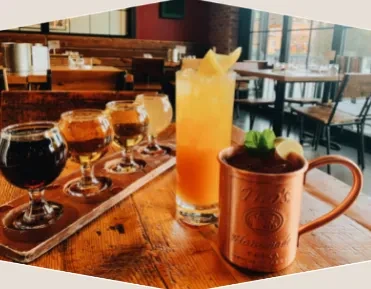 Beer flight, orange cocktail, and copper mug on a rustic table.