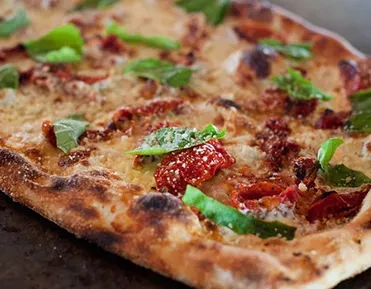 Rectangular pizza with melted cheese, sun-dried tomatoes, and fresh basil.