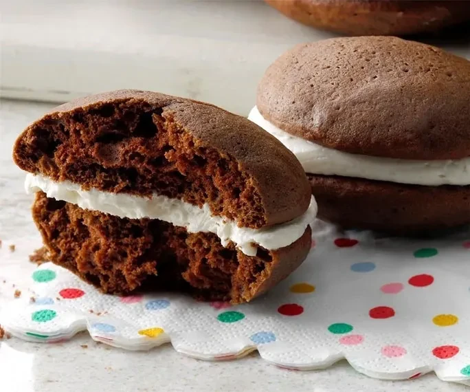 Chocolate whoopie pies with white filling, one cut open on a polka-dot napkin.