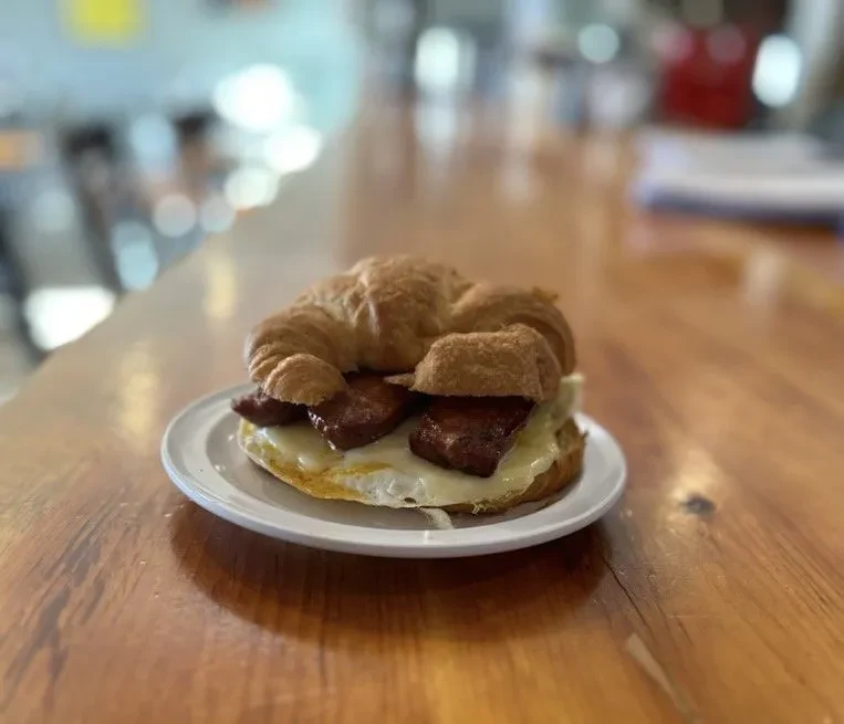 Golden-brown croissant breakfast sandwich with egg and sausage on white plate.