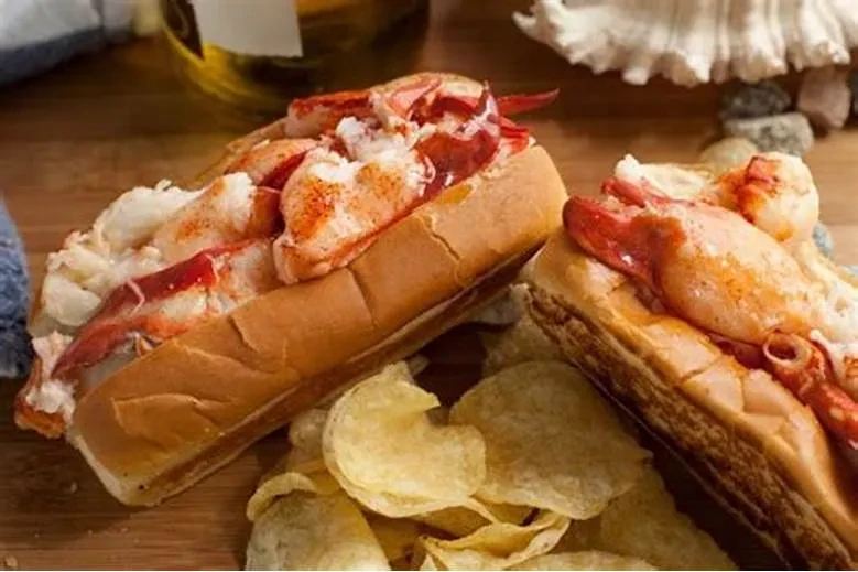 Two lobster rolls with large lobster chunks and chips on wood.