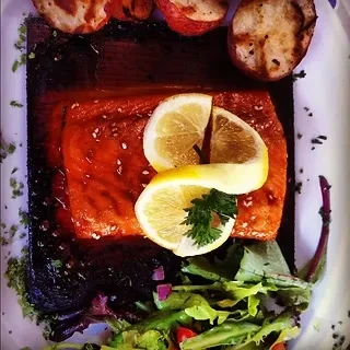 Plated cedar-planked salmon, roasted potatoes, and salad on a wooden board.