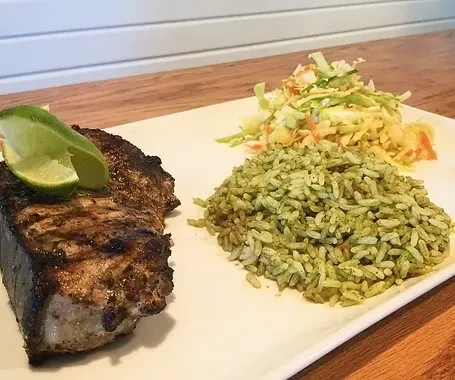 Grilled fish with char marks, green rice, and coleslaw on white plate.