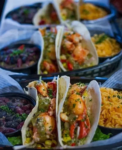 Two seafood tacos with green sauce, black beans, and yellow rice.