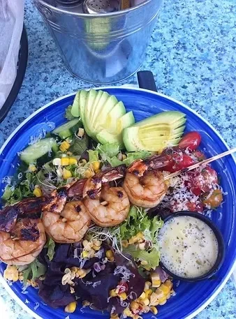 Four-skewer grilled shrimp salad with avocado and corn on blue plate.