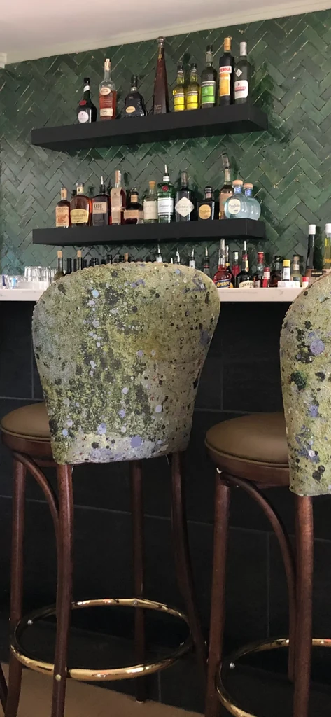 Stylish bar with green herringbone tiles, liquor display, and two stools.