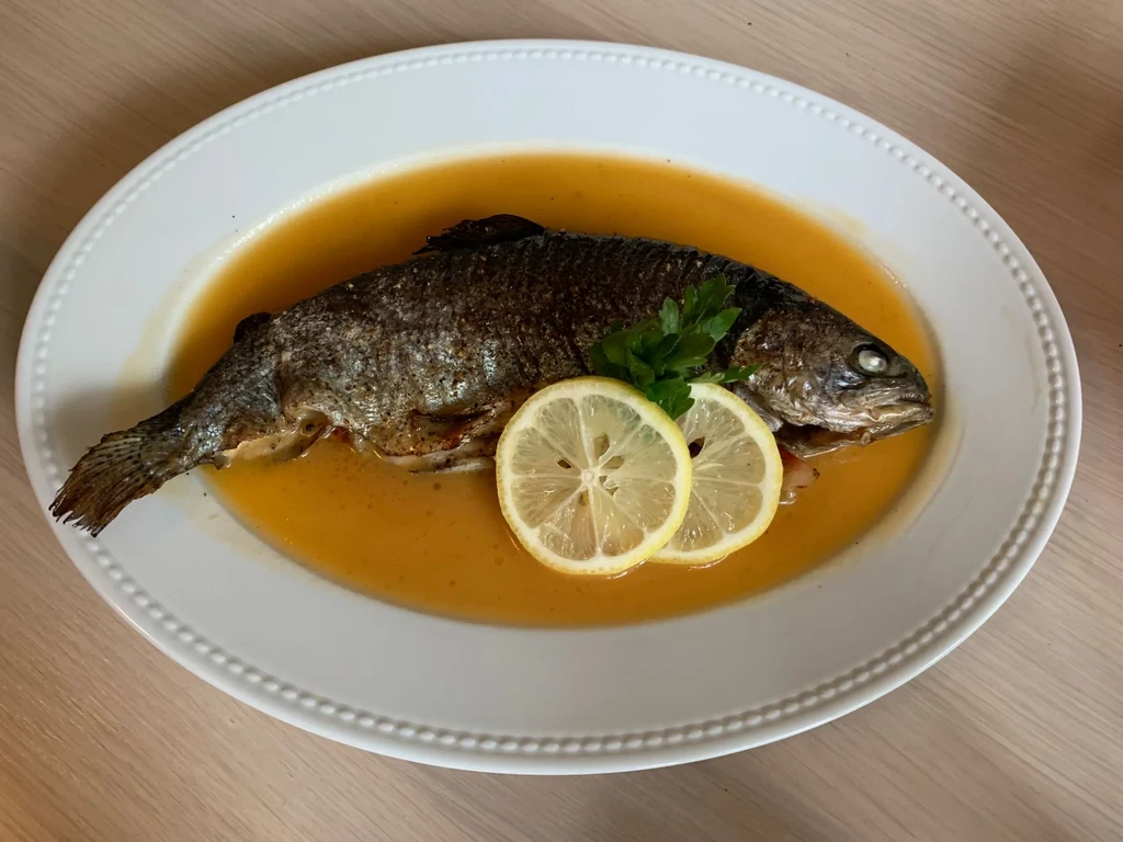 Cooked fish garnished with lemon and parsley on a white plate.