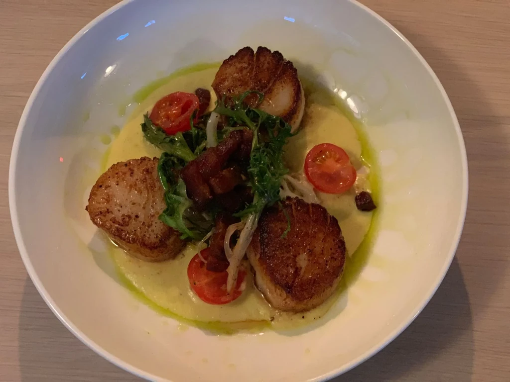 Pan-seared scallops on puree with tomatoes, greens, and crispy pork belly.