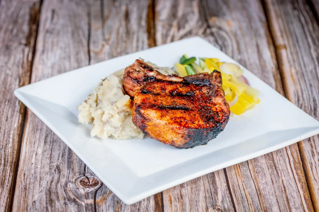 Grilled pork chop, mashed potatoes, and squash on a white plate.