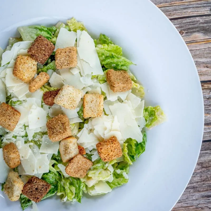 Top-down Caesar salad with romaine, Parmesan, and croutons on wood.