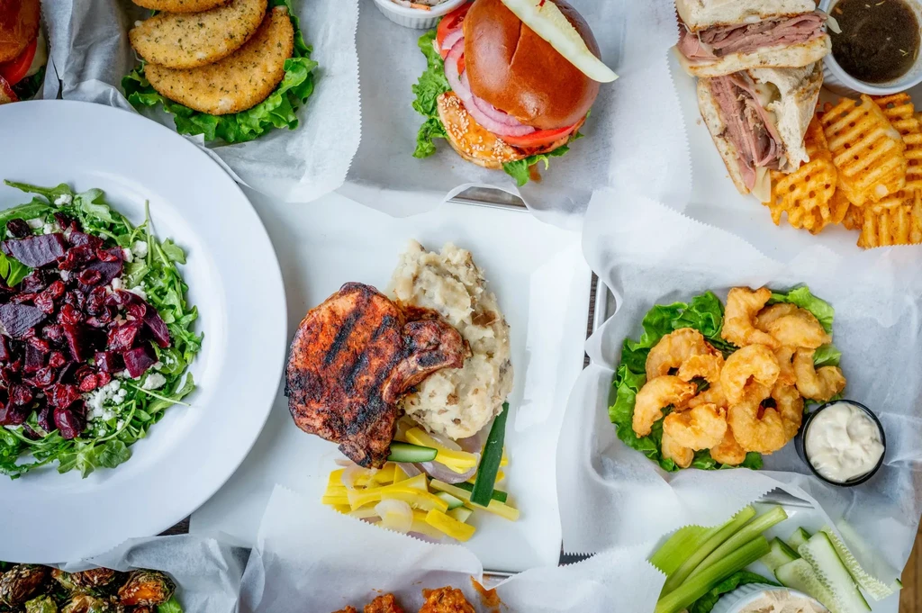 Flat-lay of many diverse plated restaurant dishes on a white surface.