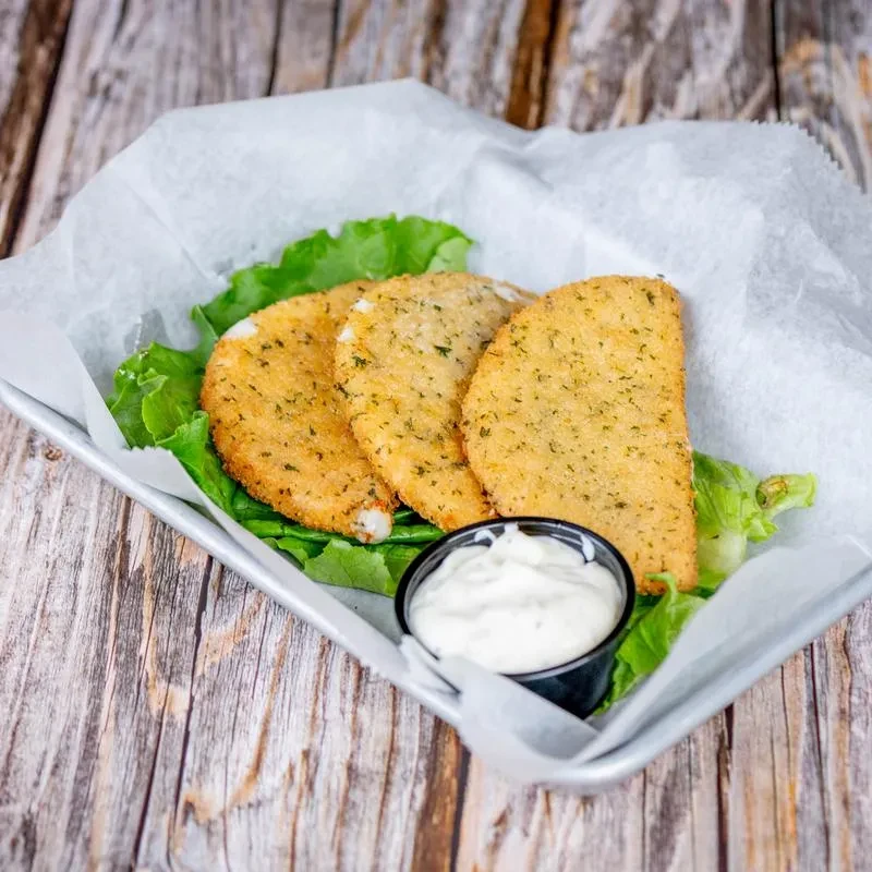 Three fried half-moon items with herb breading, lettuce, and dip.