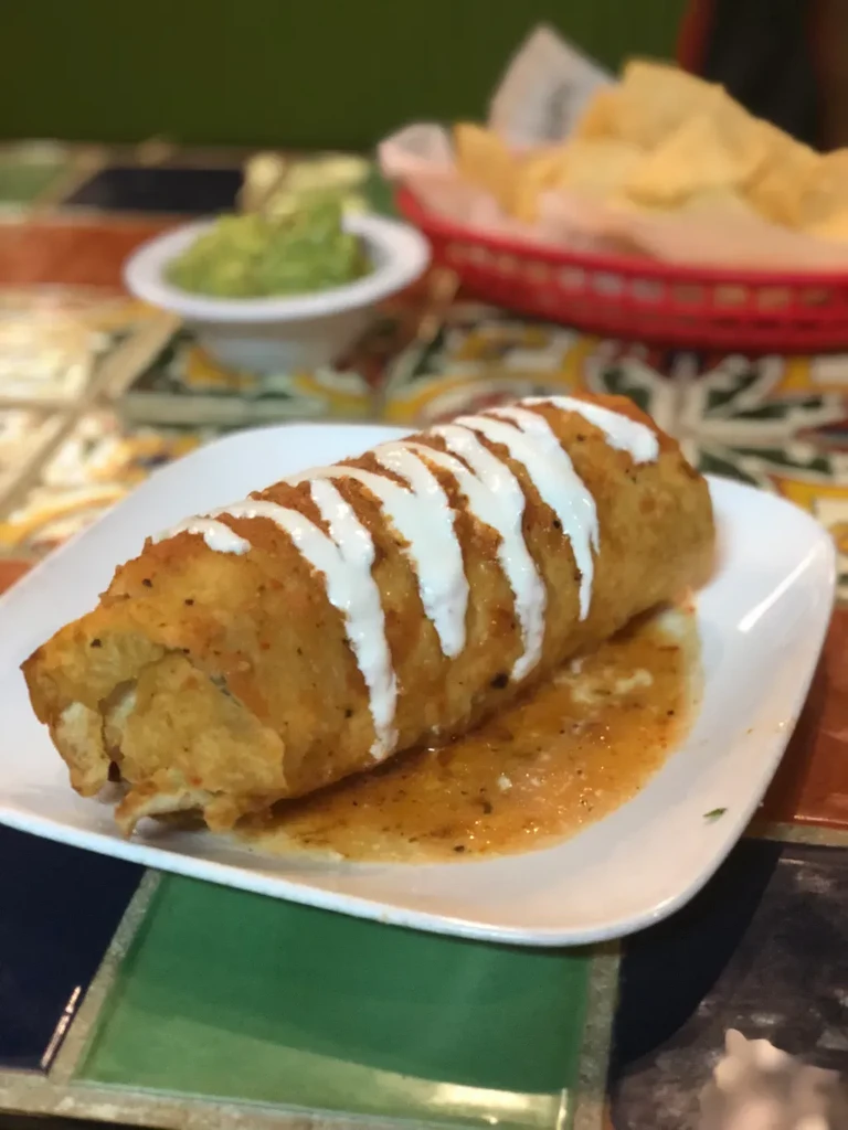 Golden chimichanga with crema, orange sauce, guacamole, and chips.