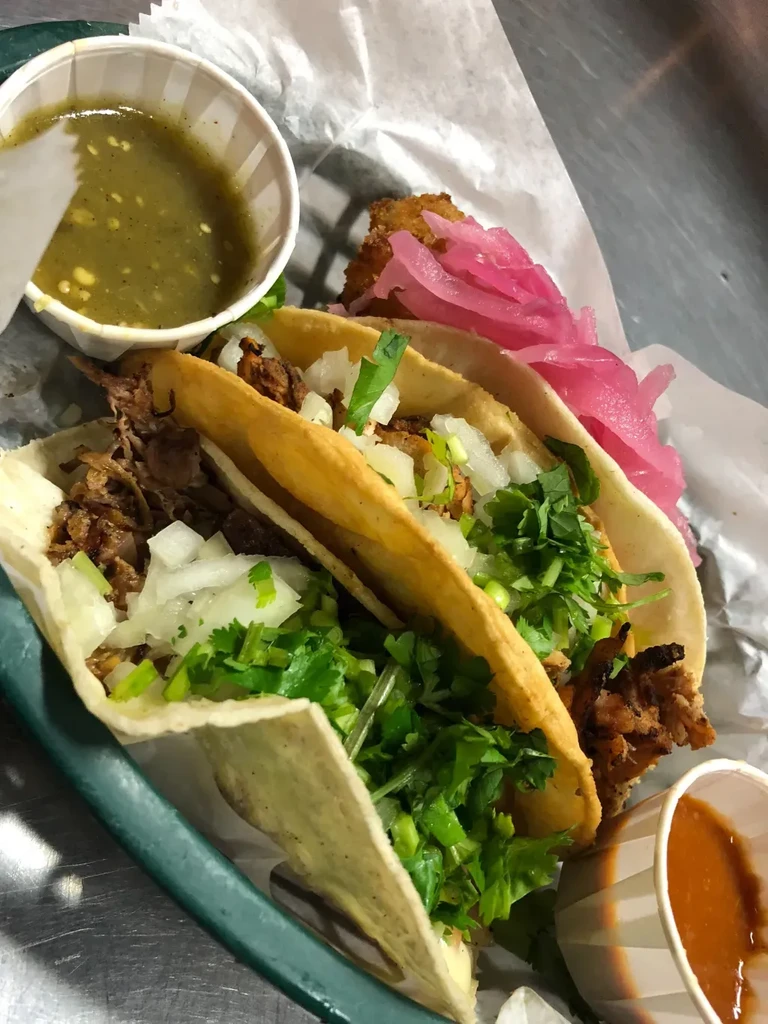 Three meat tacos with onions, cilantro, pickled onions, and two salsas.