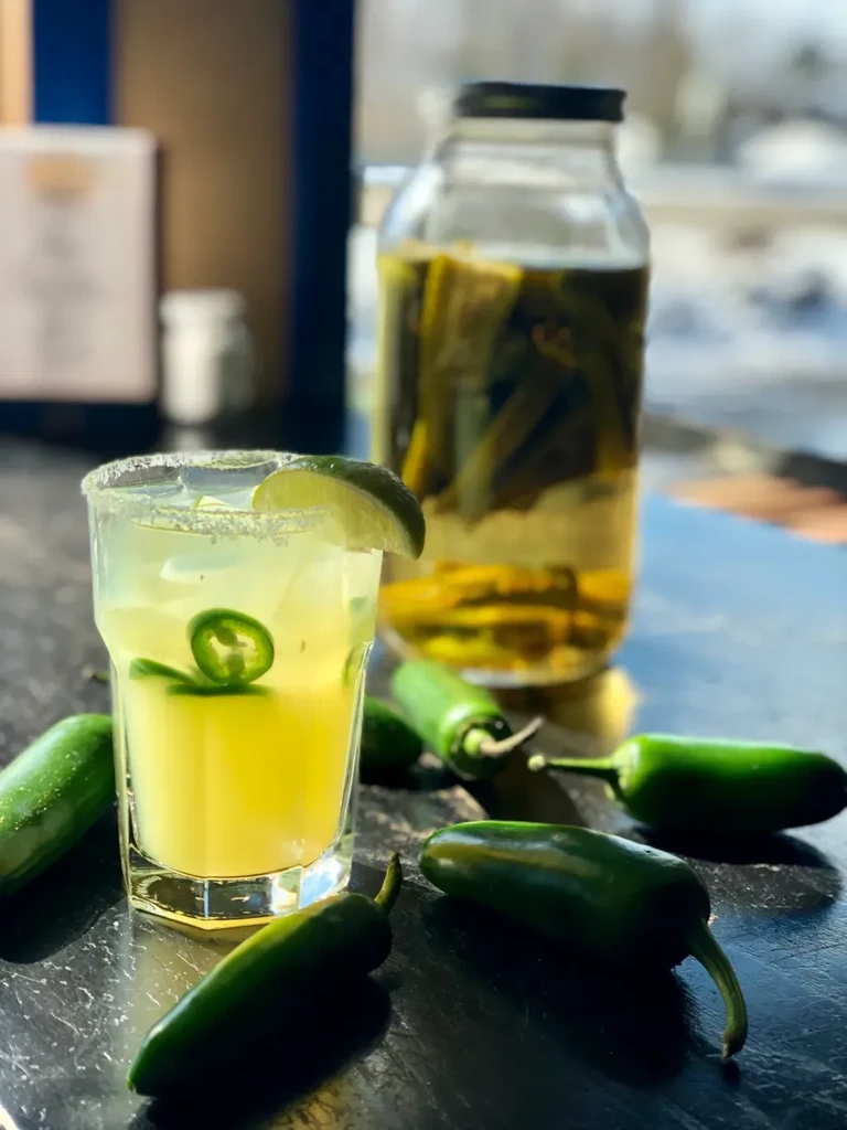 Light-yellow jalapeño margarita with salt rim, lime, and whole jalapeños.