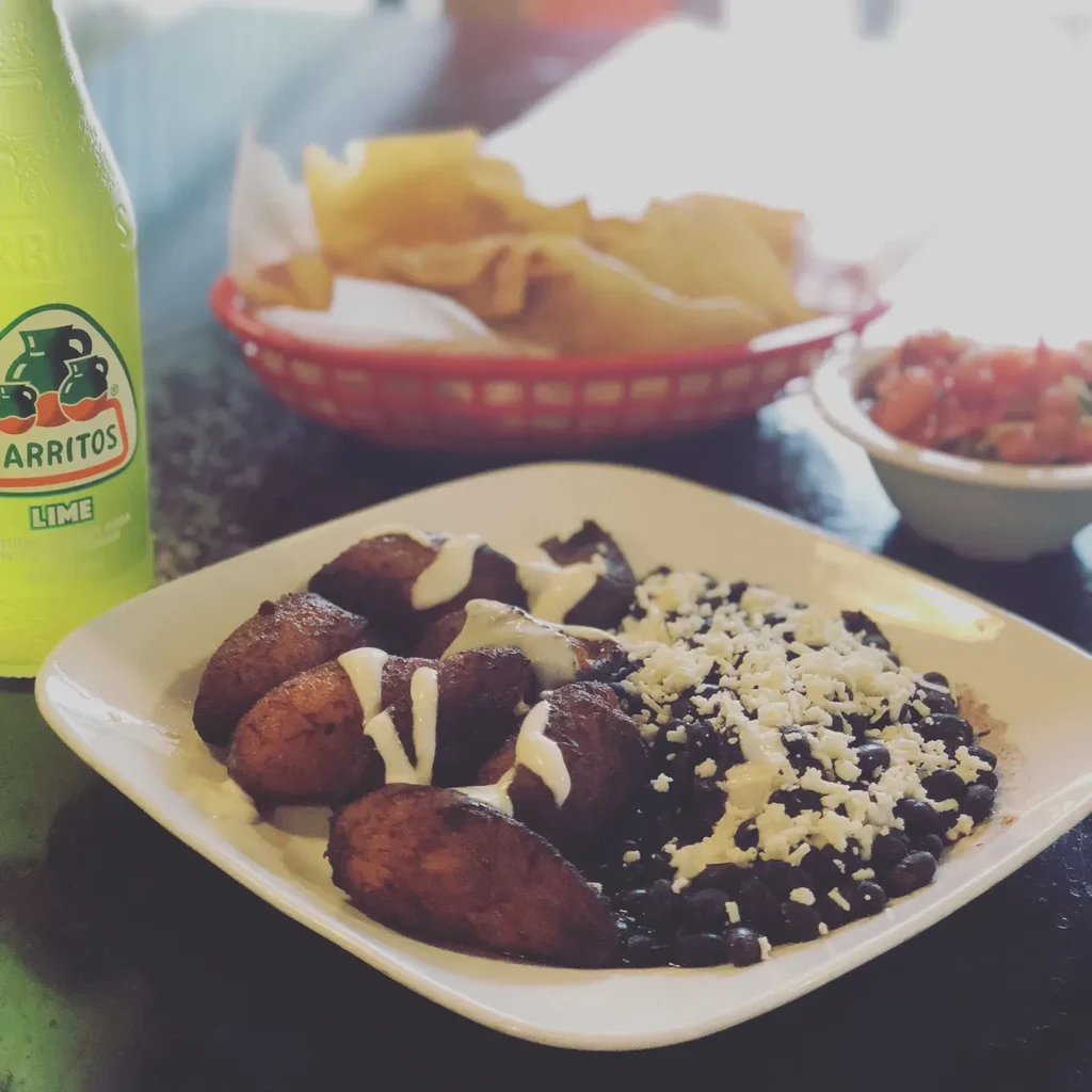 Close-up of fried plantains, black beans, cheese, and Jarritos soda.