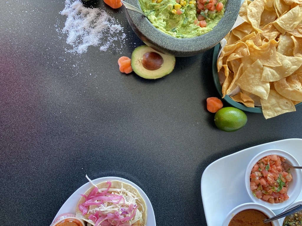 Vibrant Mexican food spread on a dark table: tacos, guacamole, chips.