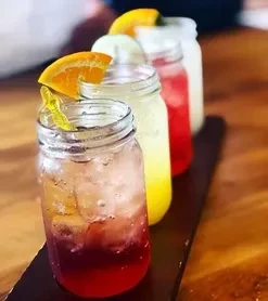 Four vibrant drinks in mason jars on a wooden board.