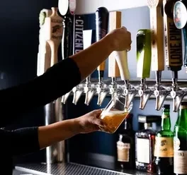 Hands pour golden beer from a tap at a well-stocked bar.