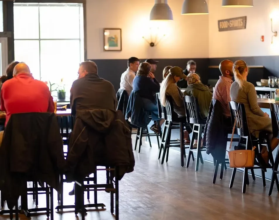 Casual restaurant interior with patrons, a bar, and 'FOOD • SPIRITS' sign.