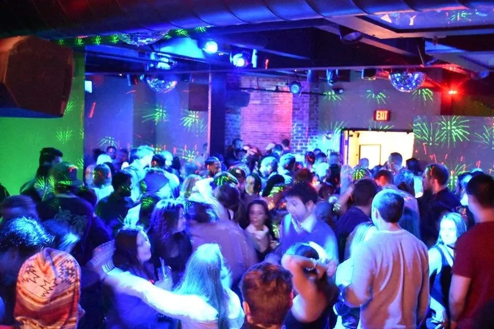 Crowded club, blue and green neon, disco balls, EXIT sign.