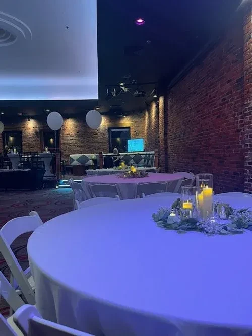 Purple-blue lit restaurant event space with candlelit tables and brick wall.