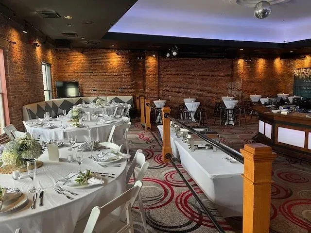 Wedding reception venue with set tables, buffet, bar, and brick walls.