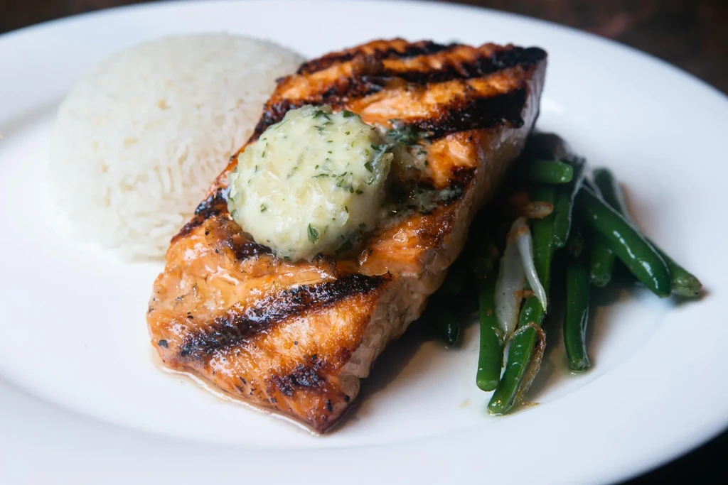 Grilled salmon with char marks, melting herb butter, rice, green beans.