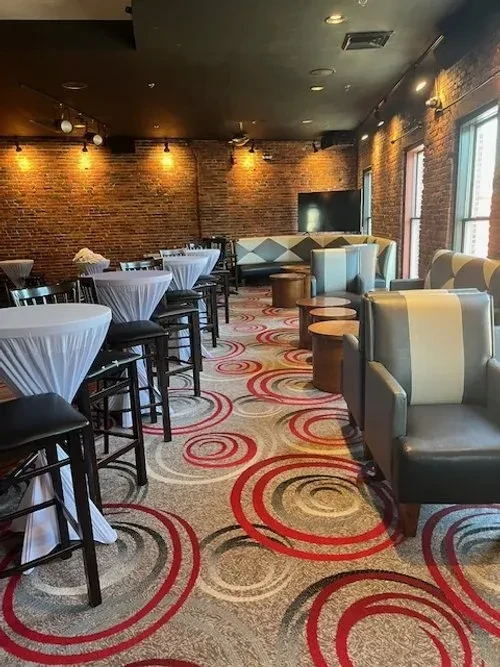 Bar lounge with brick walls, patterned carpet, high-top and lounge seating.