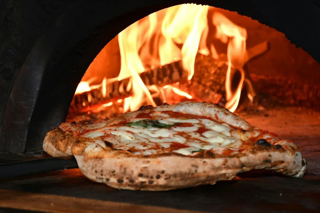 Neapolitan pizza baking in a wood-fired oven, surrounded by flames.
