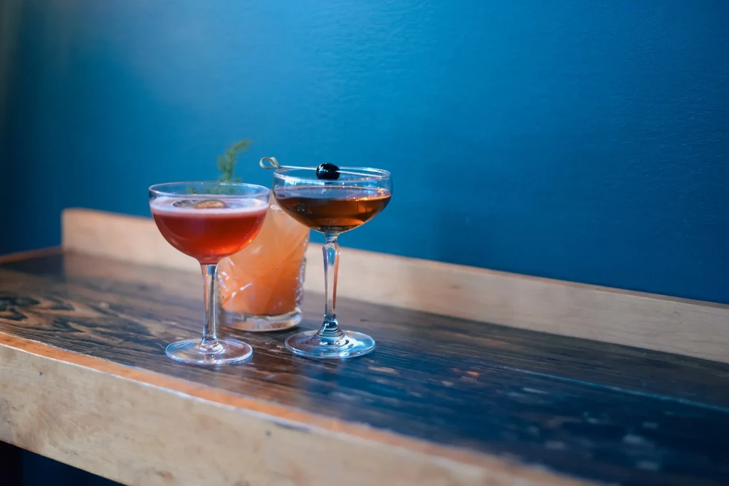 Three colorful cocktails with garnishes on a dark wooden countertop.