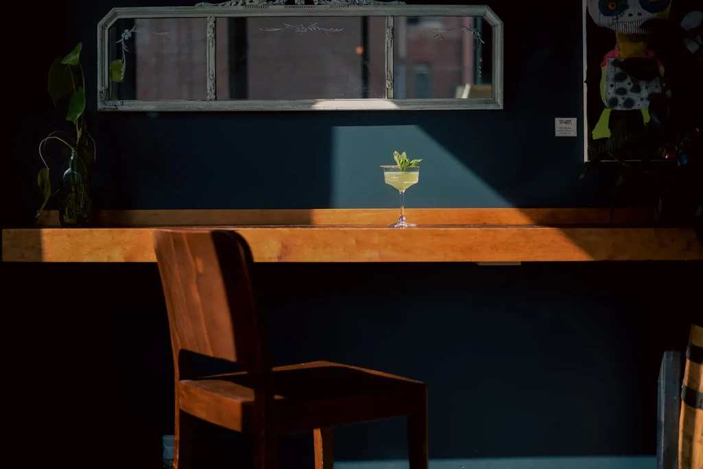 Light green cocktail with mint on wooden counter, dramatic shadows.