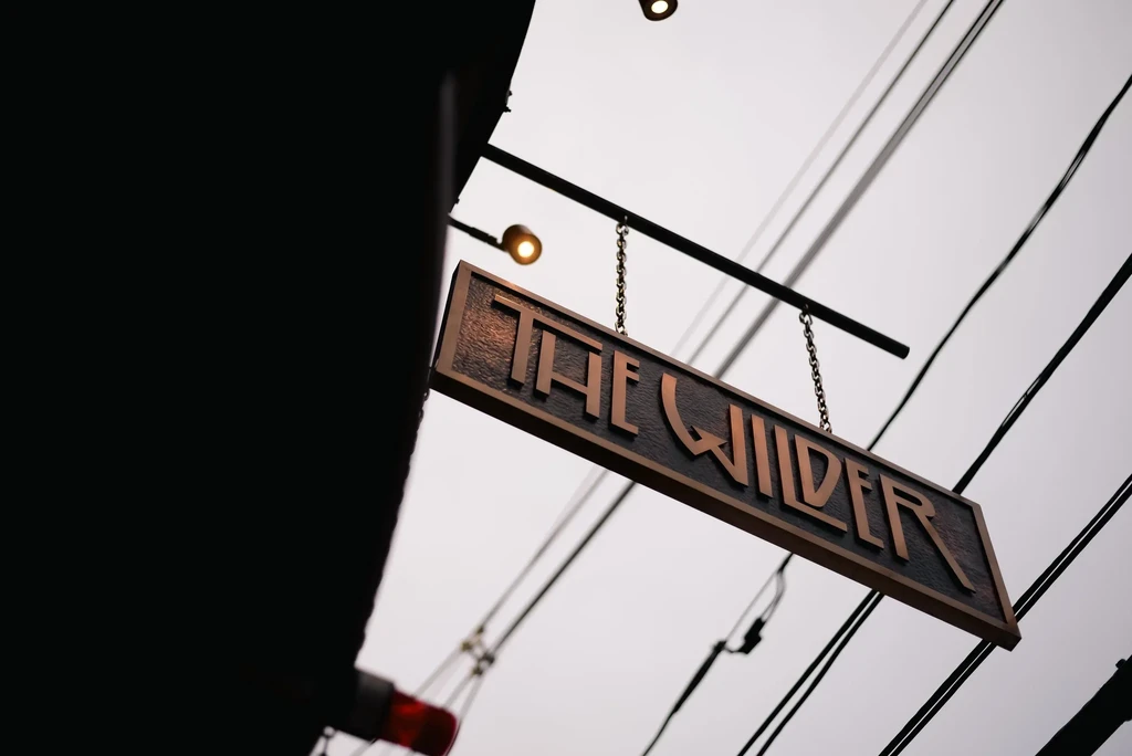 Outdoor hanging sign "THE WILDER" with raised metallic lettering.