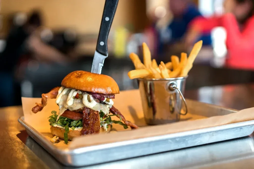 Gourmet burger and fries on a tray in a blurred restaurant setting.