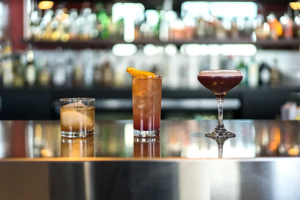 Three distinct cocktails in different glasses on a reflective bar.