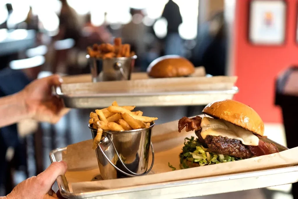 Close-up of a bacon cheeseburger and fries being served on a tray.