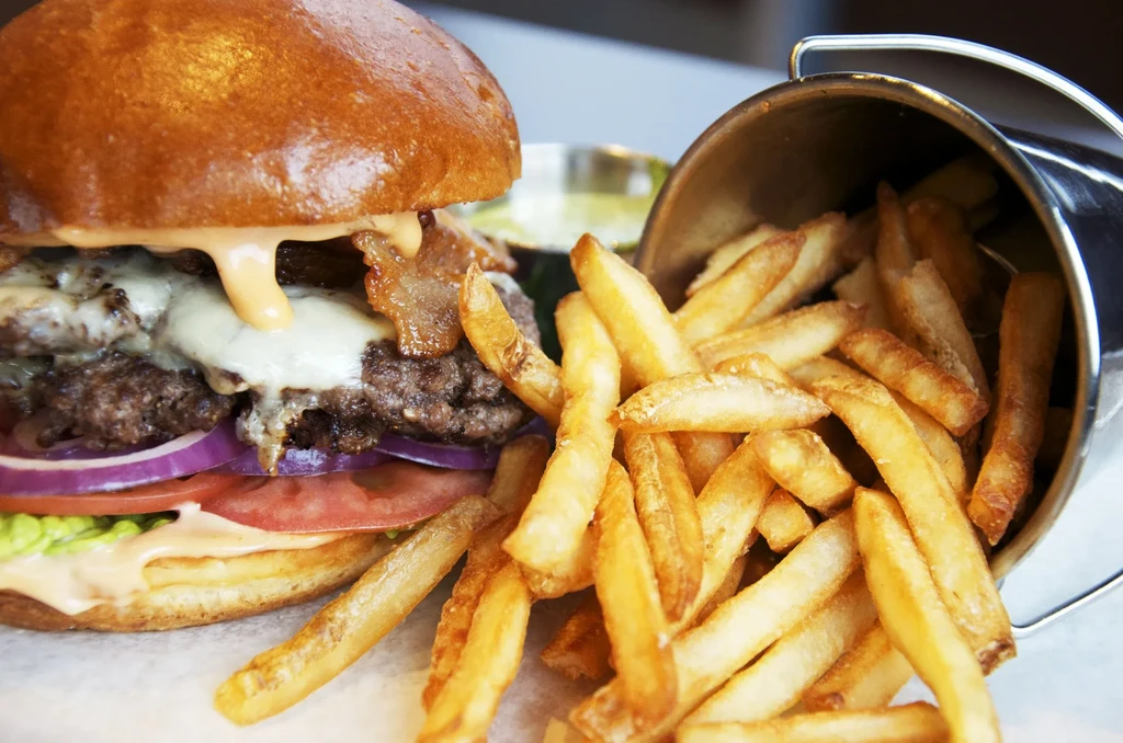 Close-up of a large stacked burger with fries spilling from a bucket.