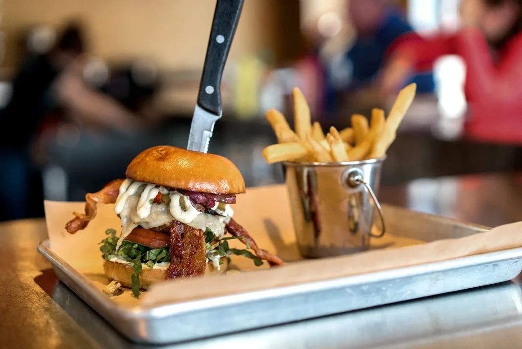 Multi-layered burger, skewered, with fries on a restaurant tray.